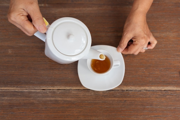 Vista superiore di un tè di versamento femminile sulla tavola di legno