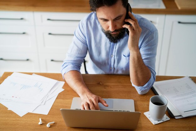 Vista superiore di un uomo che parla al telefono e usa un portatile