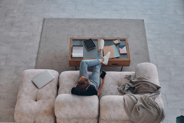 Vista superiore di una donna che usa lo smartphone mentre è seduta sul comodo divano a casa