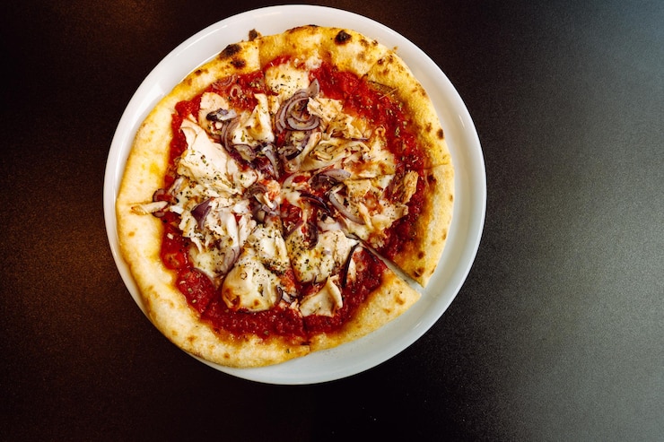 Foto vista superiore di una pizza con pollo e cipolle rosse su un piatto su un tavolo nero
