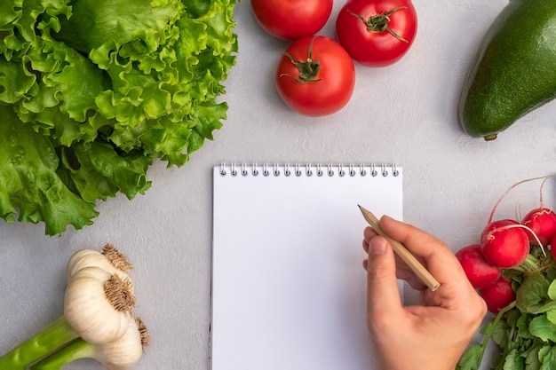 Vista superiore di verdure fresche con blocco note di carta vuoto e penna a mano della donna