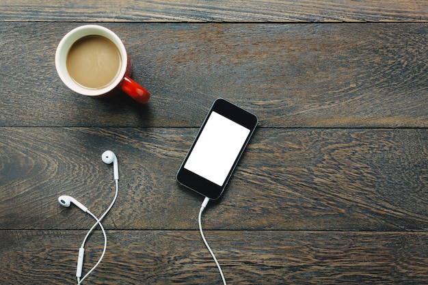 Vista superiore telefono cellulare, auricolari, caffè sul tavolo da ufficio.