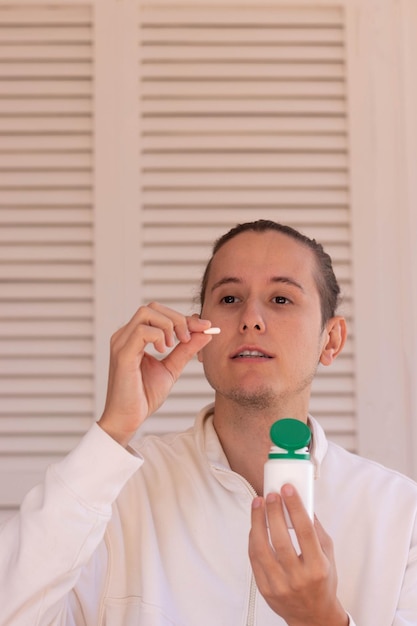 Vista verticale del giovane che sta per prendere una pillola da un contenitore bianco e verde per scopi medici