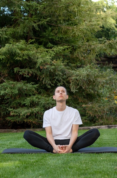 Vista verticale del giovane uomo concentrato che pratica meditazione yoga e tecnica di respirazione nella natura