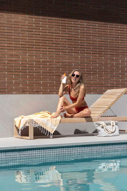 Vista verticale della giovane donna felice e sorridente mentre mostra la protezione della crema solare nell'area della piscina