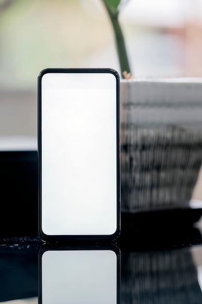 Vista verticale dello smartphone dello schermo in bianco con la pianta da appartamento sulla tavola superiore di vetro nera con il fondo della sfuocatura.