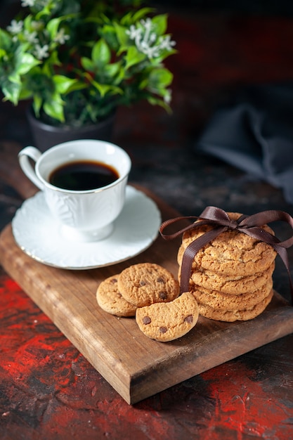 Vista verticale di delizioso caffè in una tazza bianca e biscotti di zucchero fatti in casa su un vaso di fiori di bordo di legno marrone su sfondo scuro di colori misti con spazio libero