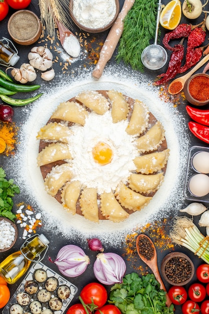 Vista verticale di gnocchi crudi su vassoio marrone con farina e set di alimenti su tavola di colore scuro