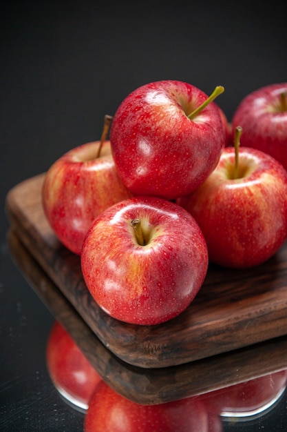 Vista verticale di mele rosse fresche su tagliere di legno su sfondo di colore scuro