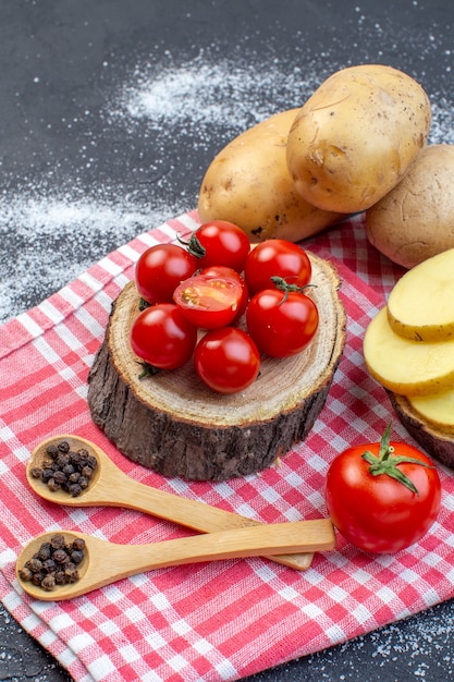 Vista verticale di patate crude intere e tritate su tavola di legno pomodori freschi su sfondo bianco nero colori misti