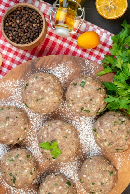 Vista verticale di polpette di carne cruda con verde in un piatto marrone e riso fresco verde limone caduto bottiglia di olio pepe su asciugamano rosso su sfondo nero