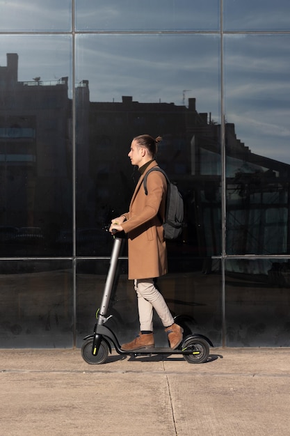 Vista verticale di un giovane bussinesman che guida uno scooter elettrico intorno al quartiere finanziario del centro città