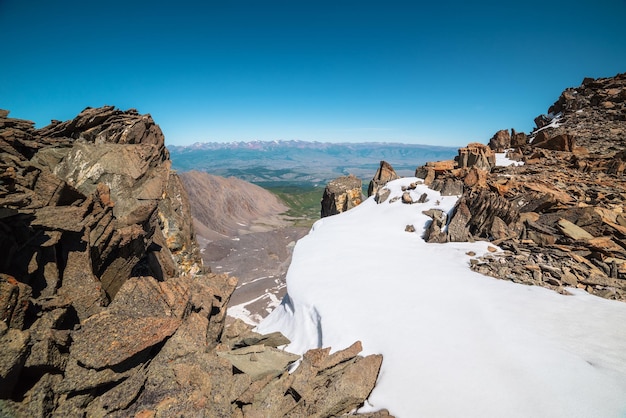 Vista vertiginosa dal bordo del precipizio con cornice innevata e ripido canale fino a una grande catena montuosa sotto il cielo blu in una giornata di sole Fantastico paesaggio con rocce affilate tra la neve vicino all'abisso ad altissima quota