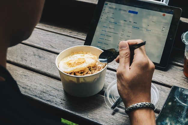 Visto da dietro un uomo asiatico che fa colazione con una ciotola di riso con uova prima di iniziare a lavorare