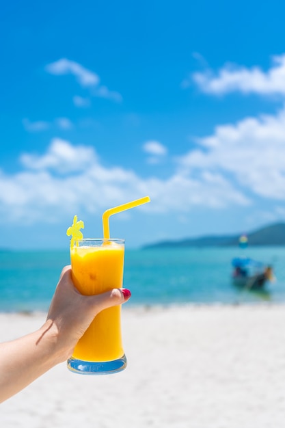 Visuale in prima persona. La ragazza tiene una tazza di vetro di mango freddo fresca sulla parete di una spiaggia tropicale di sabbia. Sabbia bianca e una barca. Vacanza da favola in Tailandia