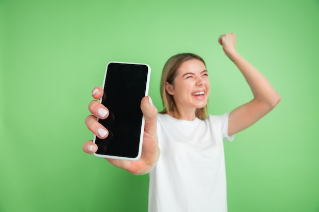 Visualizzazione dello schermo vuoto. Il ritratto della giovane donna caucasica isolato sulla parete verde. Bellissimo modello femminile in camicia bianca.