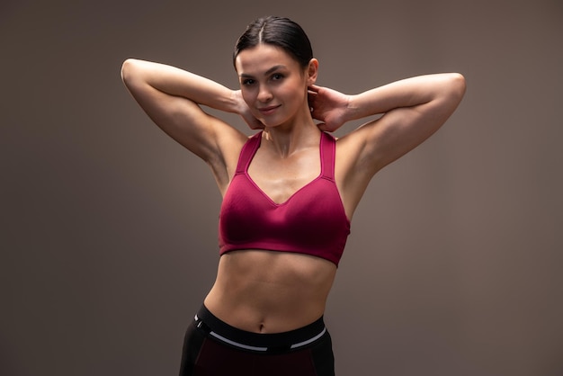 Vita verticale della donna atletica che posa alla macchina fotografica prima dell'esercizio di fitness in studio con parete marrone