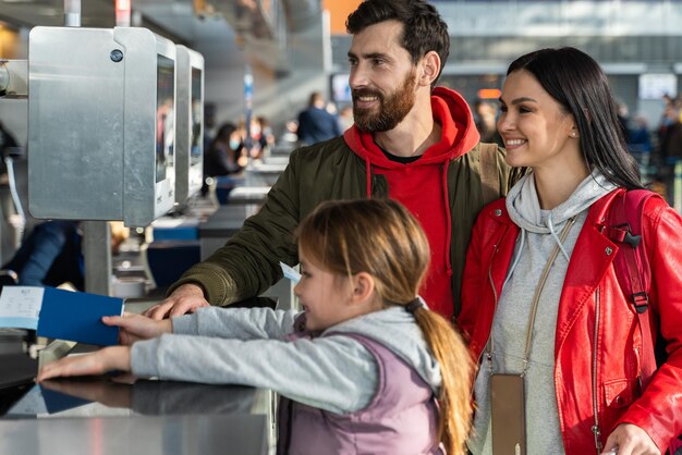 Vita verticale della madre, del padre e della figlia felicissimi che si sentono felici mentre hanno la procedura di check-in in aeroporto