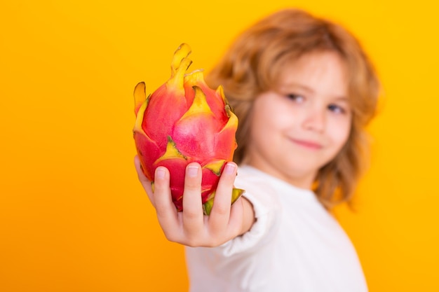 Vitamina e frutti sani per i bambini Kid tenere il frutto del drago in studio Studio ritratto di bambino carino con frutto del drago isolato su sfondo giallo