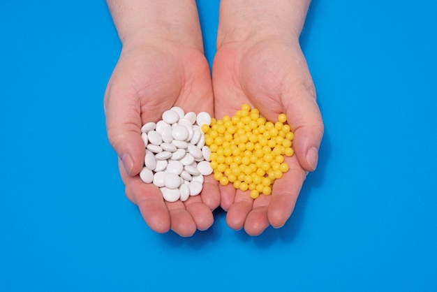 Vitamine nelle mani di un adulto compresse bianche e capsule gialle su sfondo blu