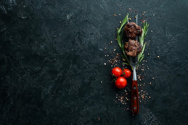 Vitello al forno su una forchetta. Bistecca di vitello su fondo di pietra nera. Vista dall'alto. Spazio libero per il tuo testo.