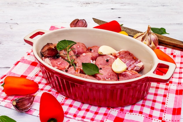 Vitello crudo tagliato a pezzi con verdure e altri ingredienti pronti da cuocere. Tavolo rustico in legno bianco, concetto culinario biologico, primi piani