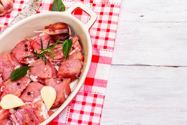 Vitello crudo tagliato a pezzi con verdure e altri ingredienti pronti da cuocere. Tavolo rustico in legno bianco, concetto culinario biologico, vista dall'alto