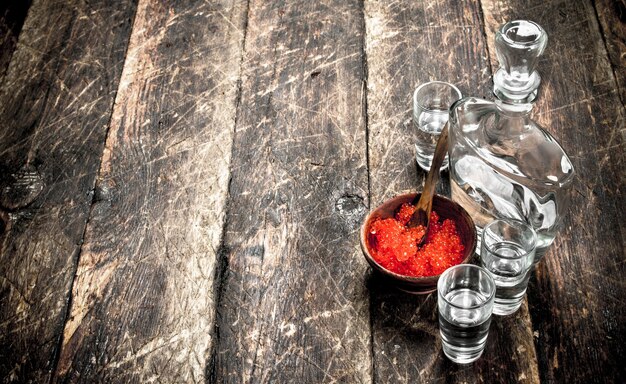 Vodka in una bottiglia con caviale nero e rosso. Sullo sfondo di legno.