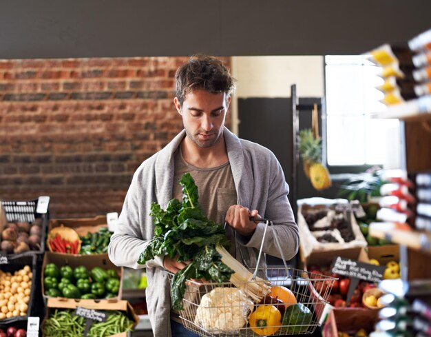 Voglio solo lo scatto più fresco di un giovane che cammina in un negozio di alimentari con un cesto pieno di prodotti freschi