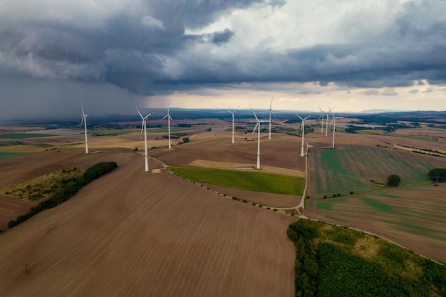 Volo del drone ad alta quota su un grande campo con molte turbine eoliche che girano Le turbine eoliche proiettano una lunga ombra perché il sole sta tramontando Sullo sfondo del cielo tempestoso