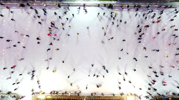 Volo di vista aerea del drone su molte persone in abiti colorati che pattinano su una pista di pattinaggio all'aperto in inverno