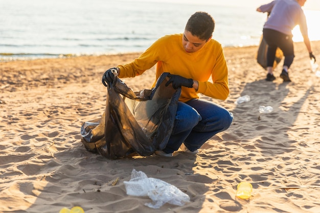 Volontari per la Giornata della Terra attivisti raccolgono la spazzatura pulizia della spiaggia zona costiera donna e uomo mette