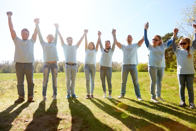 volontariato, beneficenza e concetto di persone - gruppo di volontari felici che si tengono per mano all'aperto