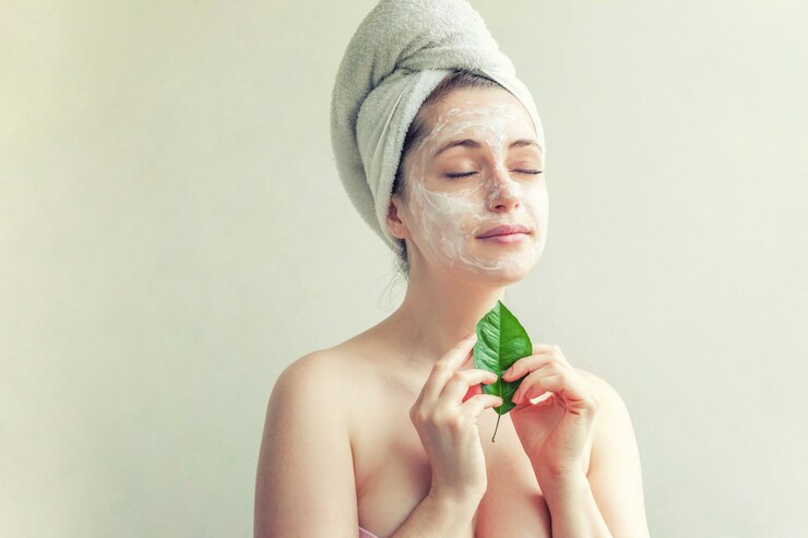 Volto di donna con foglia verde e crema o maschera nutriente
