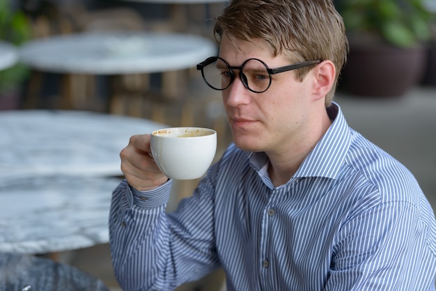 Volto di giovane uomo d'affari biondo con gli occhiali che beve caffè presso la caffetteria