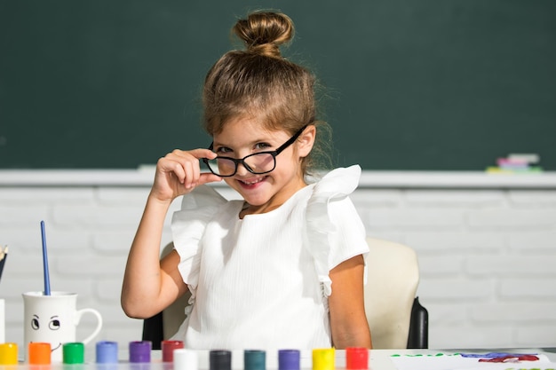 Volto di ragazza carina della scuola con gli occhiali Bambine che disegnano immagini colorate con pastelli a matita nell'aula scolastica Dipingere i bambini