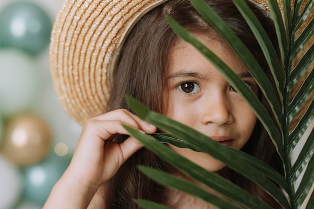 Volto di una bambina circondata da foglie tropicali Concetto di bellezza per la cura della pelle dei cosmetici naturali