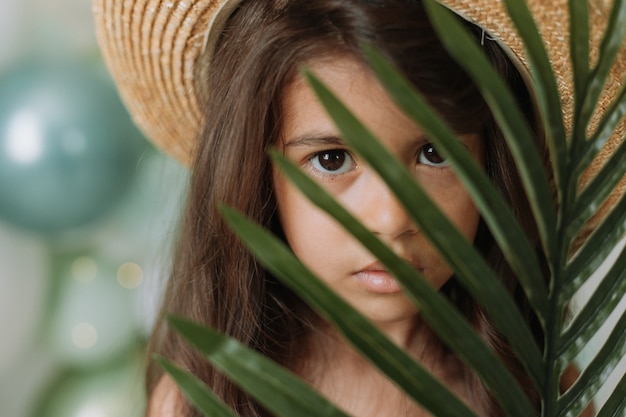 Volto di una bambina circondata da foglie tropicali Ritratto in primo piano di un bellissimo bambino bruno