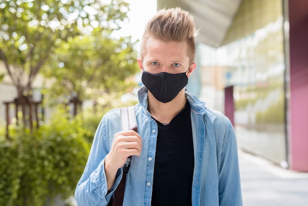 Volto di uomo con zaino che indossa la maschera nelle strade della città all'aperto