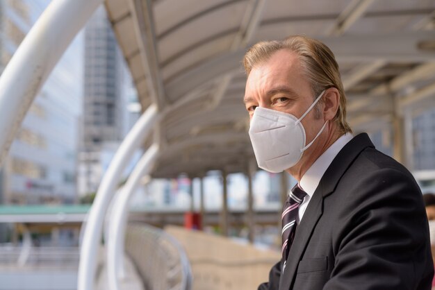 Volto di uomo d'affari maturo con maschera pensando e guardando la vista della città