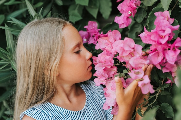 Volto ritratto di candida bambina di otto anni su sfondo di piante verdi e ammirato godetevi l'odore dei fiori rosa durante un concetto di salute mentale di viaggio di vacanza estiva gen z