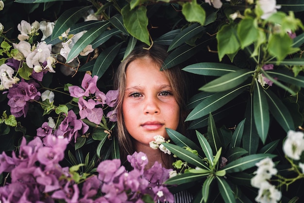 Volto ritratto di candida bella bambina di otto anni con occhi marroni verdi su sfondo di piante verdi e fiori rosa durante un viaggio di vacanza estiva gen z concetto di salute mentale