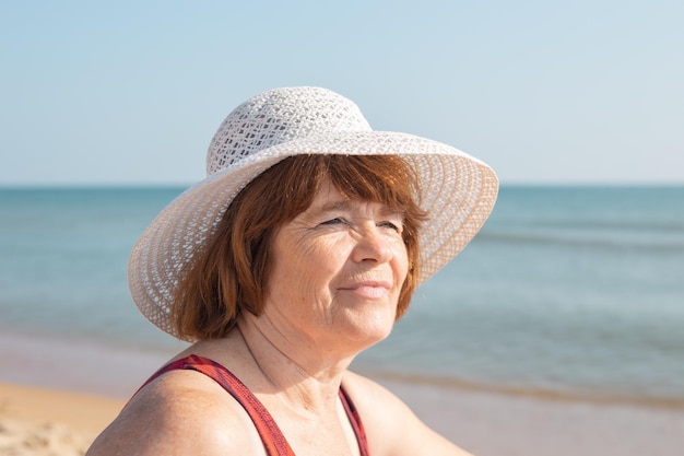 Volto soddisfatto di una donna anziana con un cappello in riva al mare in una giornata di sole closeupFelice giornate estive