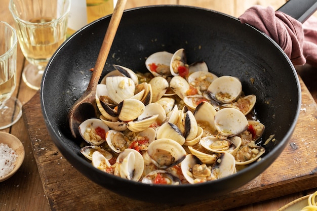 Vongole casalinghe fresche appetitose saporite alle vongole con aglio e vino bianco sulla pentola. Avvicinamento.