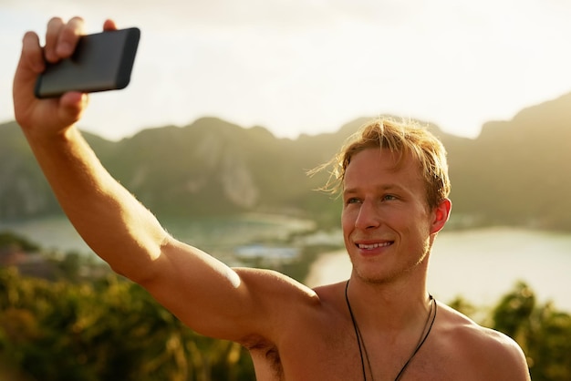 Vorrei che tu fossi qui Scatto di un giovane uomo felice che si fa un selfie con il cellulare mentre è in vacanza