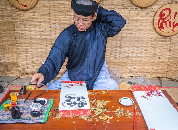 Vung Tau VIETNAM 7 GENNAIO 2023 Lo studioso vietnamita che indossa Ao Dai scrive calligrafia Il festival della calligrafia è una tradizione popolare durante le vacanze di Tet Scrivere distici per il Festival di Primavera del nuovo anno