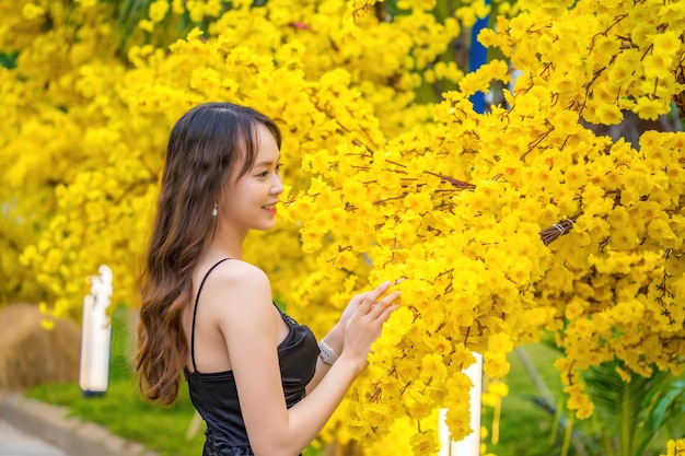 Vung Tau VIETNAM 7 GENNAIO 2023 Ritratto di una bella donna asiatica in abito nero in piedi vicino a Ochna Integerrima fiore Tet vacanze Capodanno lunare