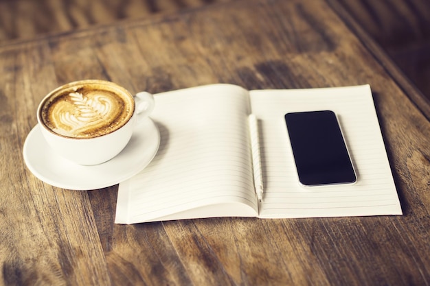 Vuoto cellulare tazza di caffè e diario su un tavolo di legno