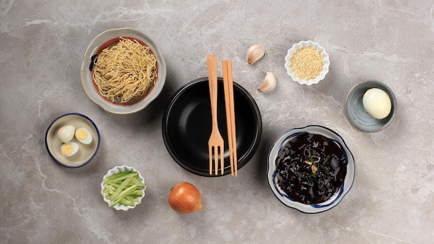 Vuoto Ttukbaegi piatto laico concetto ingredienti di Jajangmyeon o Jjajangmyeon coreano noodle con salsa di fagioli neri su cemento grigio sullo sfondo di legno