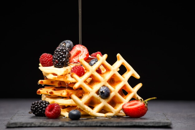 Wafer viennesi con frutti di bosco che versano miele su sfondo nero vuoto